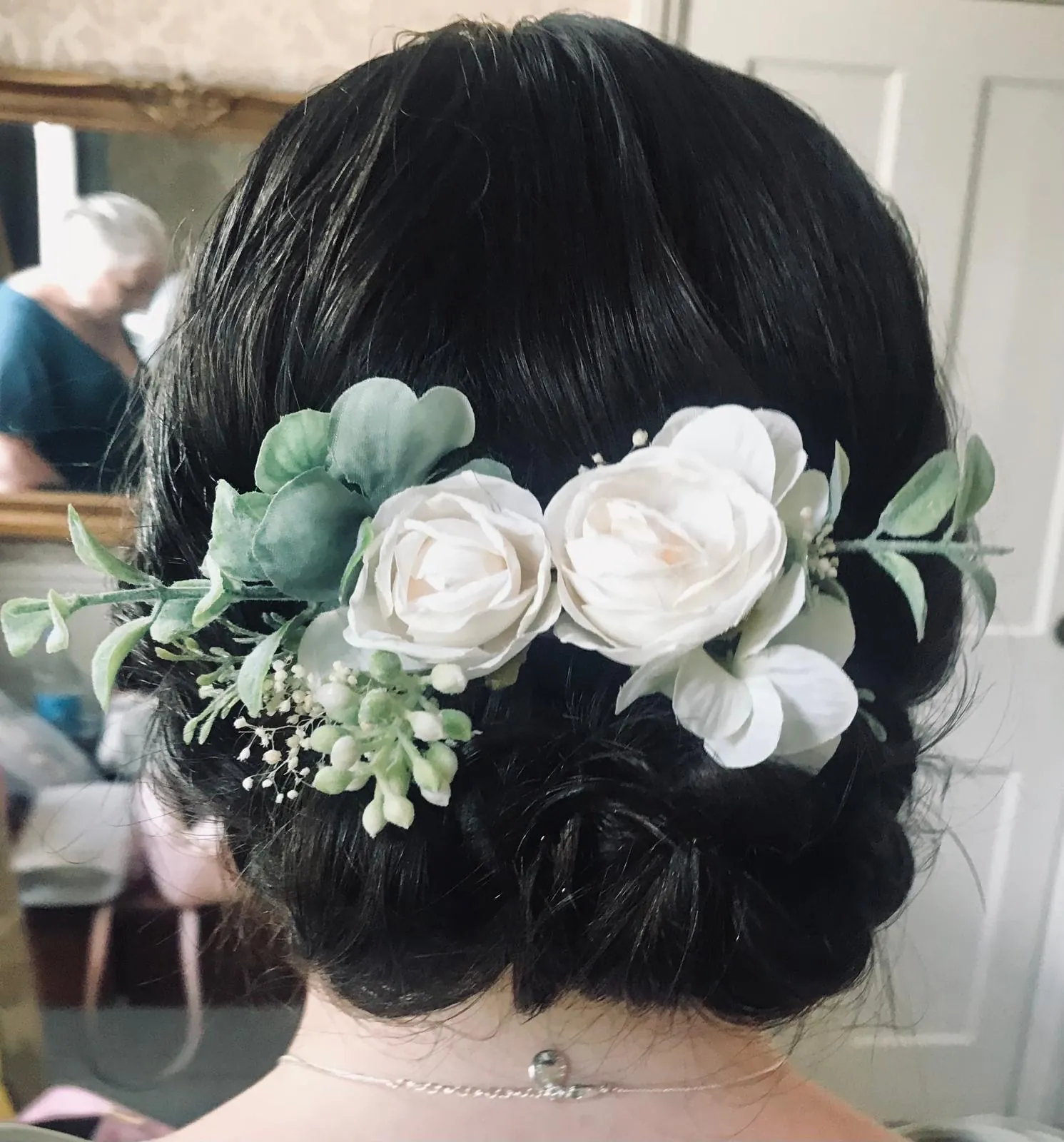 Low bridal chignon finished with white silk roses and foliage
